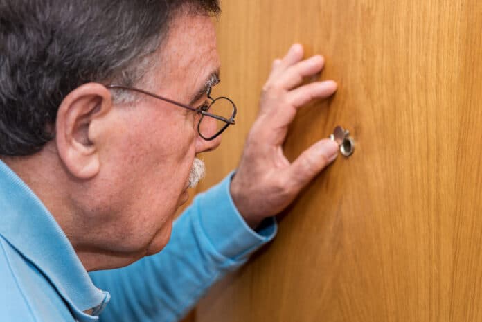 (Symbolfoto) Senior guckt durch Türloch