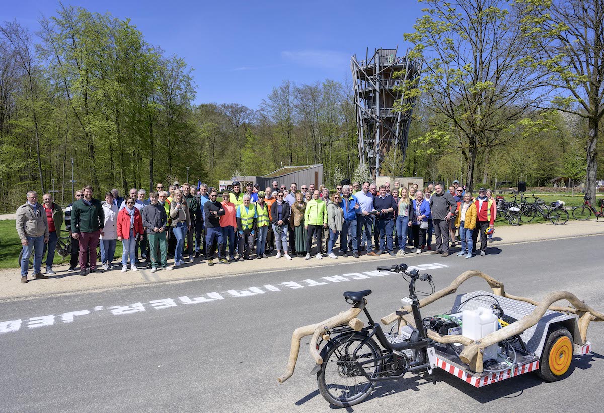 Rund 60 Radfahrende begutachten den Schriftzug des Friedensfahrrads vor dem großen Turm des Baumwipfelpfades in Bad Iburg.