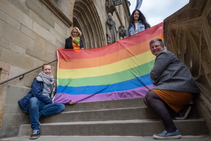 Oberbürgermeisterin Katharina Pötter (oben links), Heba Najdi vom Antidiskriminierungsbüro der Stadt Osnabrück (oben rechts), Ann Kristin Schneider, stellvertretende Gleichstellungsbeauftragte und Patricia Heller, Gleichstellungsbauftragte, mit der Regenbogenflagge, die am Dienstag, 17. Mai, an der Stadtbibliothek weht. / Foto: Monika Nestmann